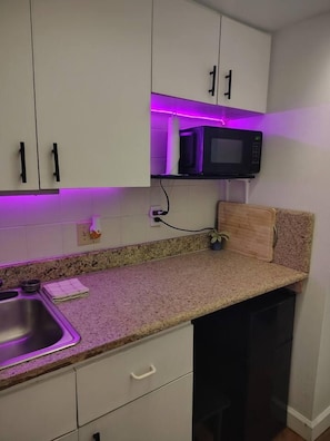 A kitchen with white cabinets, a granite countertop, a microwave, and a sink.