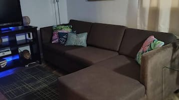 Ein Wohnzimmer mit einem braunen Ecksofa, einer schwarzen Unterhaltungsecke und einem gerahmten Bild an der Wand.