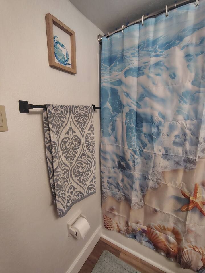 Ein Badezimmer mit einem gemusterten Handtuch auf einem Haken, einem Toilettenpapierhalter und einem Duschvorhang mit Meeresmotiven.