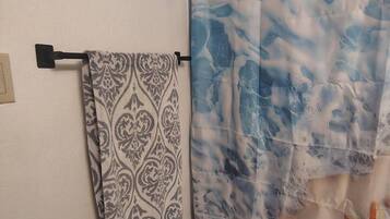 Ein Badezimmer mit einem gemusterten Handtuch auf einem Haken, einem Toilettenpapierhalter und einem Duschvorhang mit Meeresmotiven.