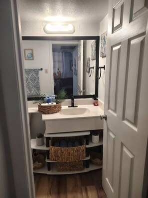 Un baño con un lavabo blanco, un espejo y un estante con cestas.
