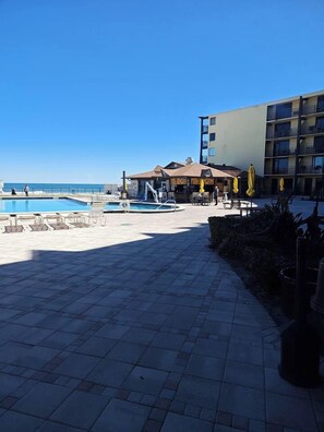 A hotel courtyard with a swimming pool, outdoor seating, and a building with multiple balconies.