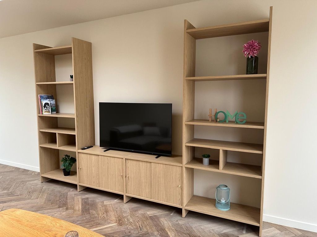 Una sala de estar moderna con televisor de pantalla plana, estanterías de madera y piso con patrón de espiga.