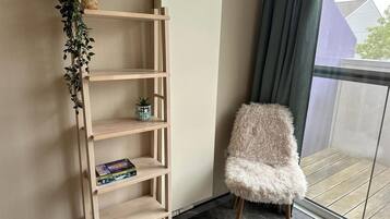 A corner of a room with a wooden bookshelf, a fluffy chair, and a window with a view of a building.