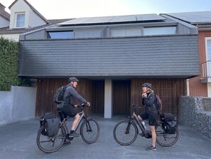 Two bicycles parked in front of a modern building with a sloped roof and large windows.