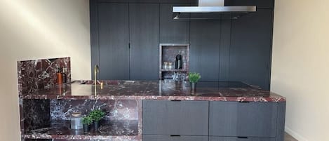 A modern kitchen with dark cabinetry, a marble countertop, and a built-in stove.