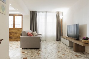 Ein modernes Wohnzimmer mit einem grauen Sofa, einem Flachbildfernseher auf einem Holzgestell und einem gemusterten Boden.