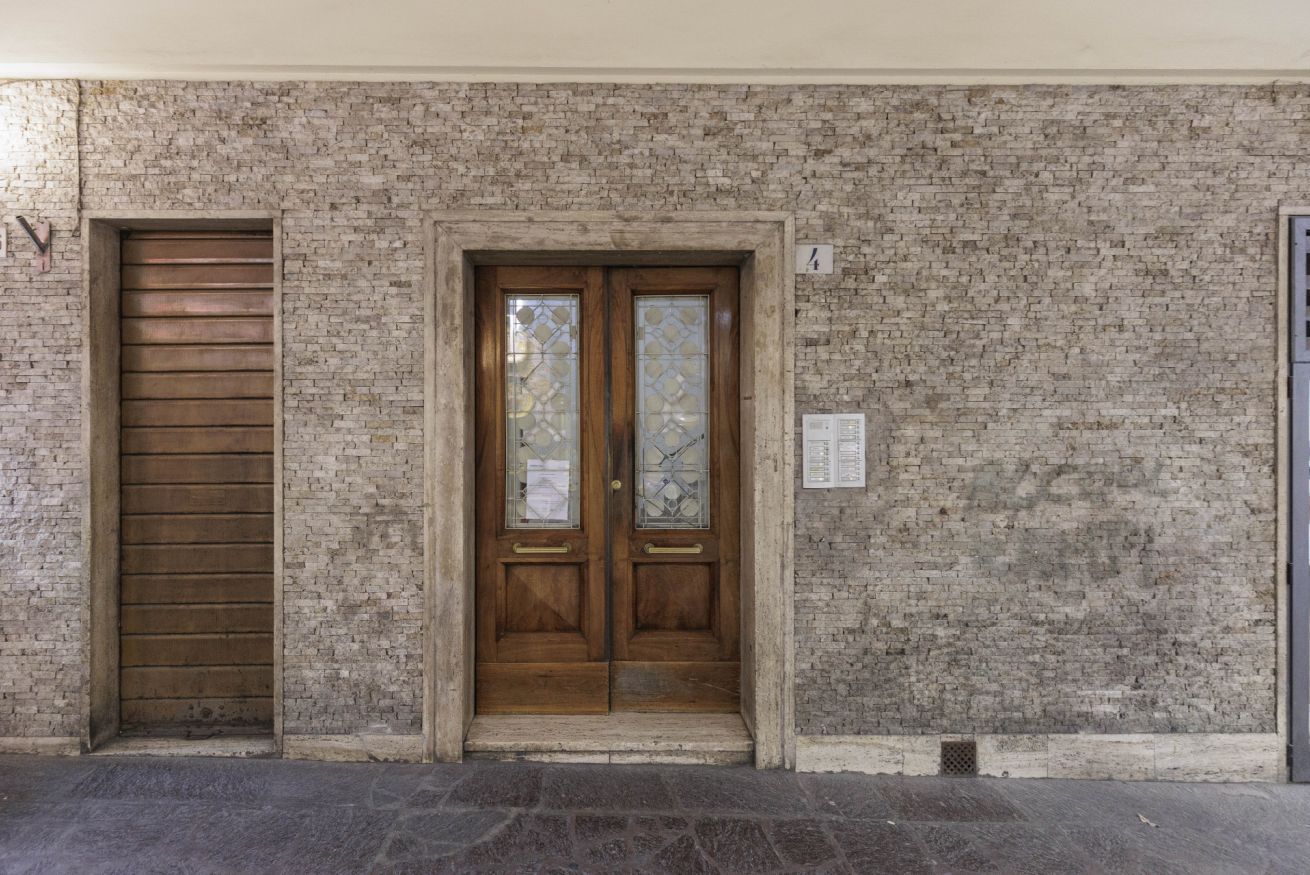 Une entrée d’immeuble avec une porte en bois et un volet métallique.