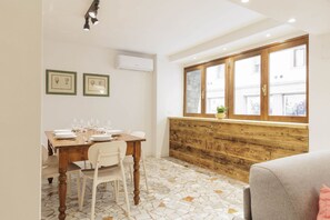 Ein Essbereich mit einem Holztisch, gedeckt für vier Personen, weißen Stühlen, einem Fenster mit Blick auf Gebäude und einer Wand-Klimaanlage.