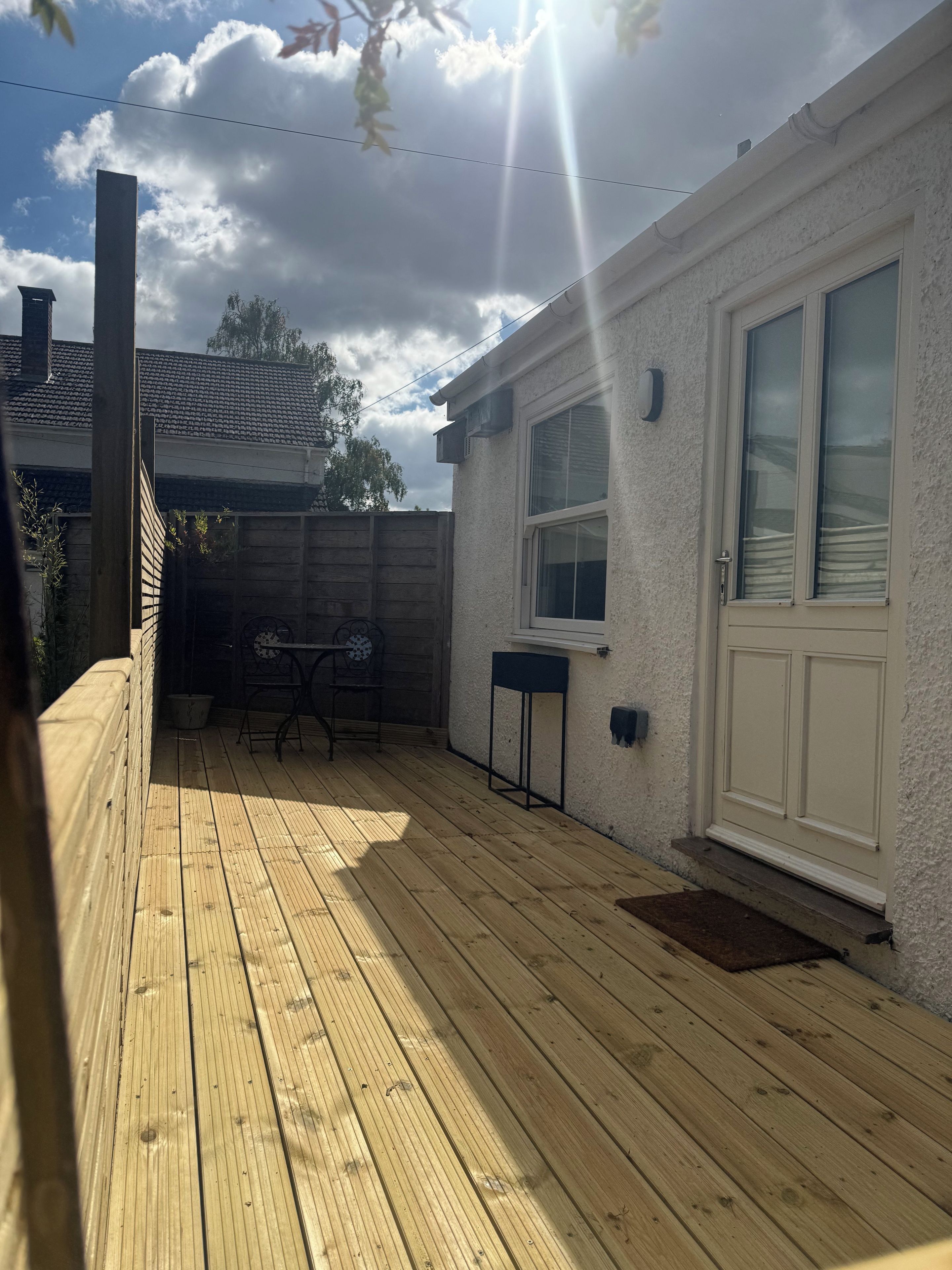 A wooden deck with a table and chairs, a white building with a window, and a wooden fence.