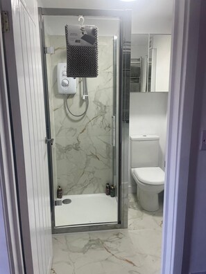 A bathroom with a glass-enclosed shower, a toilet, and a marble floor.