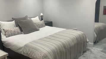 A neatly arranged bedroom with a large bed, a bedside table, a lamp, and a mirror.