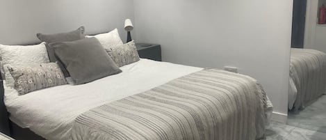 A neatly arranged bedroom with a large bed, a bedside table, a lamp, and a mirror.