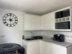 A modern kitchen with white cabinets, a black clock, a coffee maker, and a microwave on the countertop.