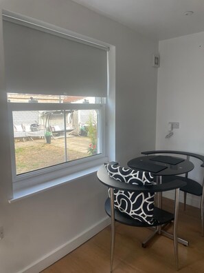 A room with a large window, a round table with a black and white patterned chair, and a white wall.