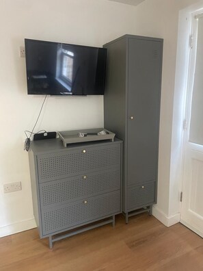A grey metal cabinet with a flat-screen TV mounted above it, a small table on top, and a door to the right.
