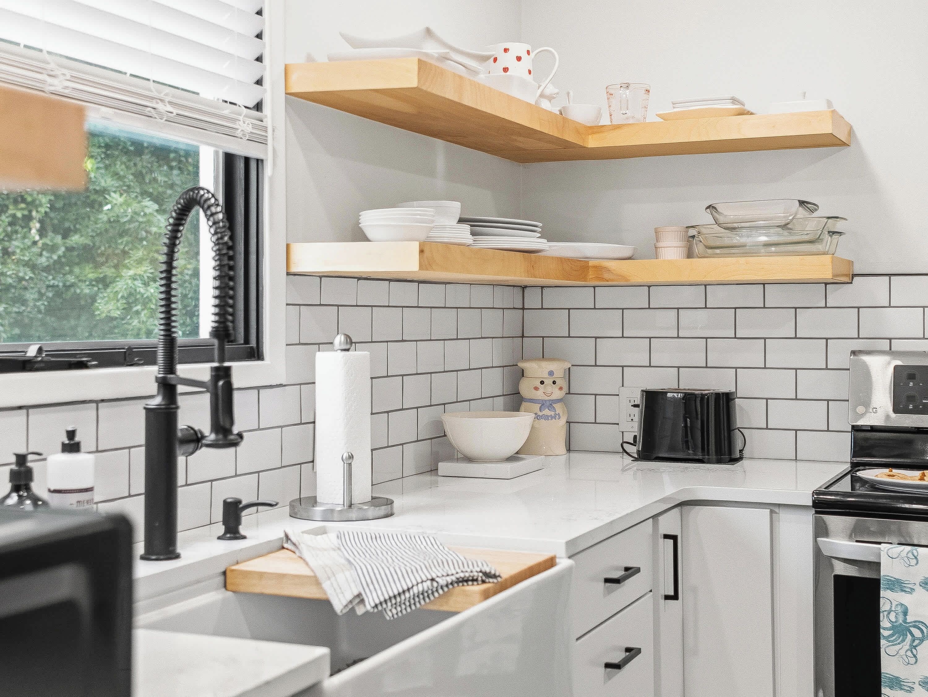 A modern kitchen with white tiles, wooden shelves, and a window.