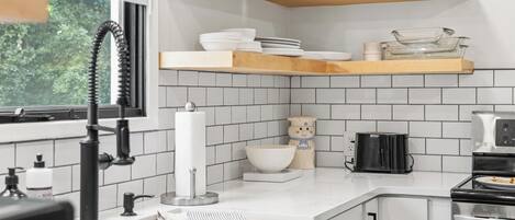 A modern kitchen with white tiles, wooden shelves, and a window.