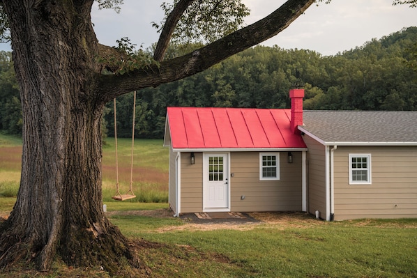 A house with a red roof, a white door, and a large tree in the foreground.