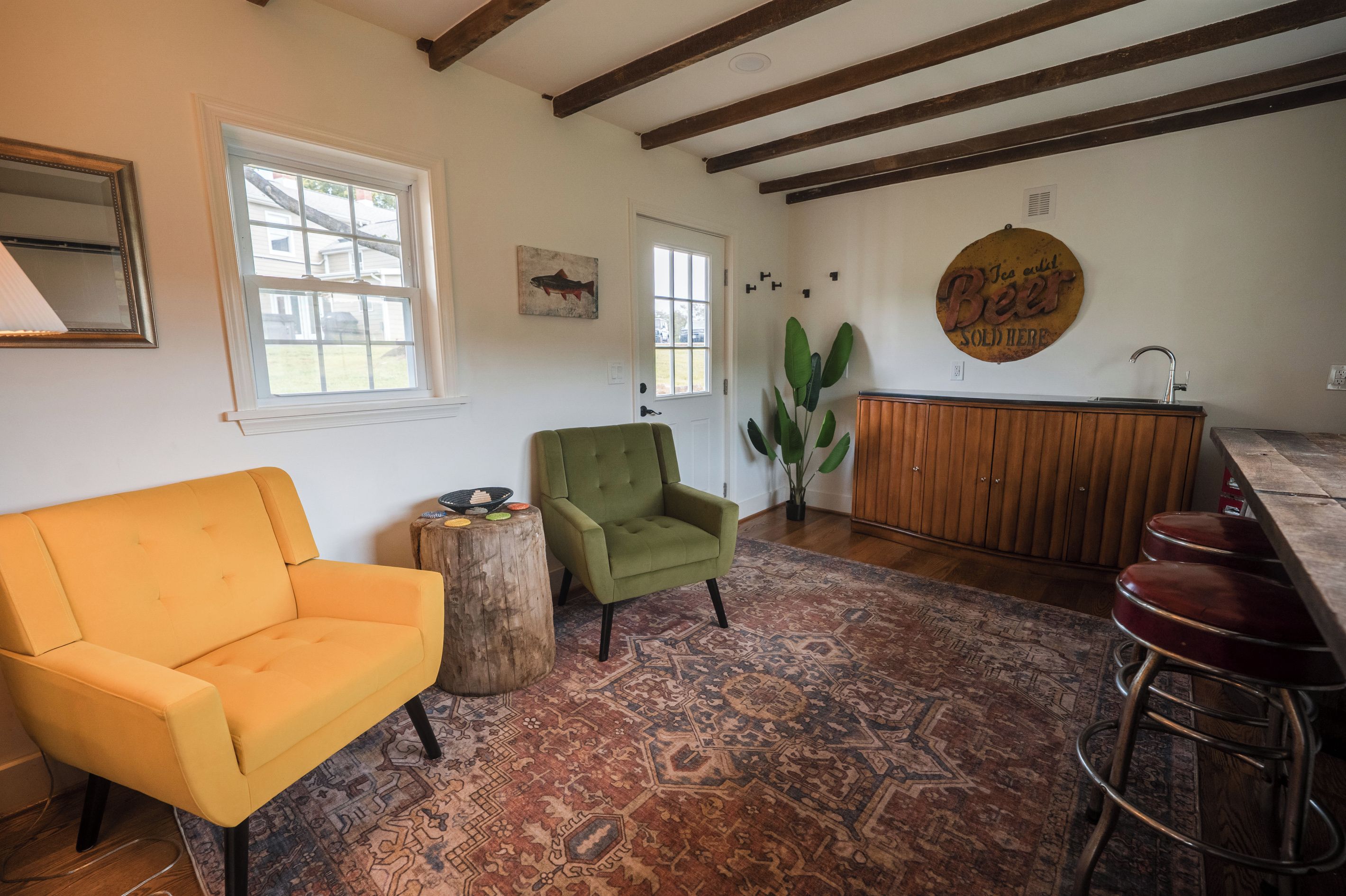 Un salon avec un canapé jaune, un fauteuil vert, un meuble en bois et un coin bar.