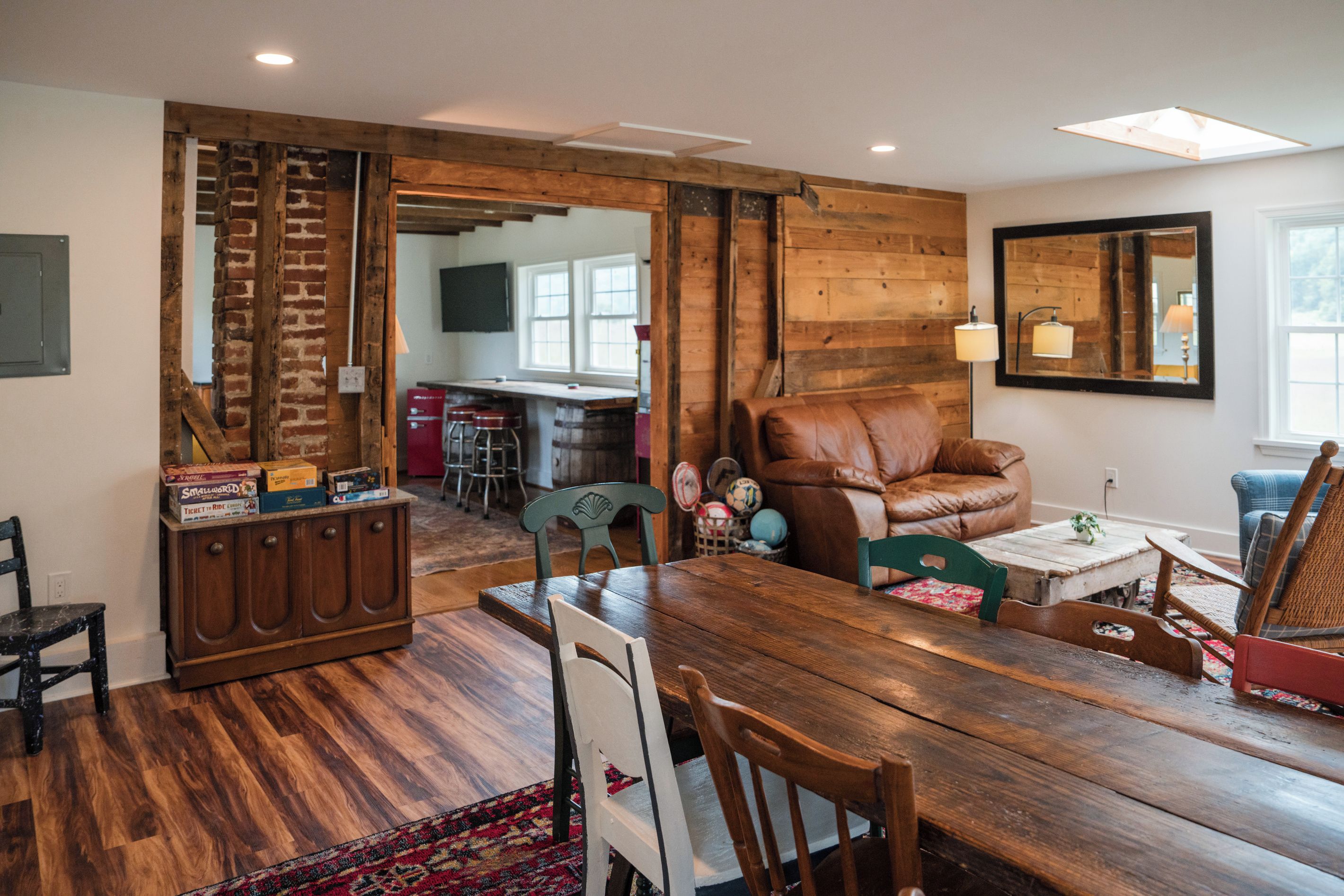 A spacious living area with a wooden dining table, a leather sofa, and a kitchen in the background.