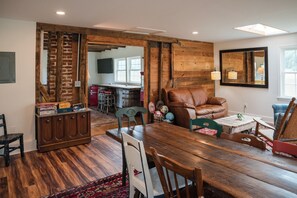 A spacious living area with a wooden dining table, a leather sofa, and a kitchen in the background.
