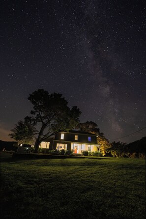 A house with a large tree in front, under a starry night sky.