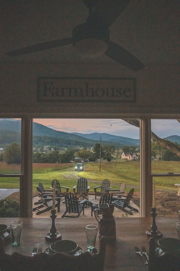 A dining area with Adirondack chairs and a table, overlooking a scenic landscape with mountains and a road.