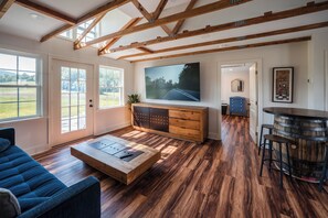 Un salon spacieux doté d’un grand téléviseur, de parquet et d’un plafond haut avec des poutres apparentes.