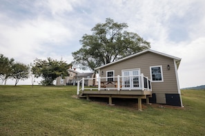 A single-story house with a deck and a large tree in the background.