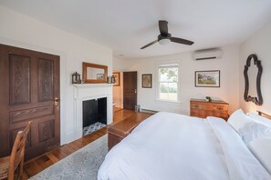 A bedroom with a bed, a fireplace, a ceiling fan, and a window.