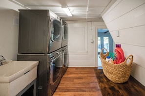 A laundry room with stacked washers and dryers, a sink, and a basket with cleaning supplies.