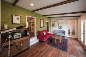 A room with a wooden floor, a red sofa, a grey armchair, a small rug, and a telescope on a tripod.