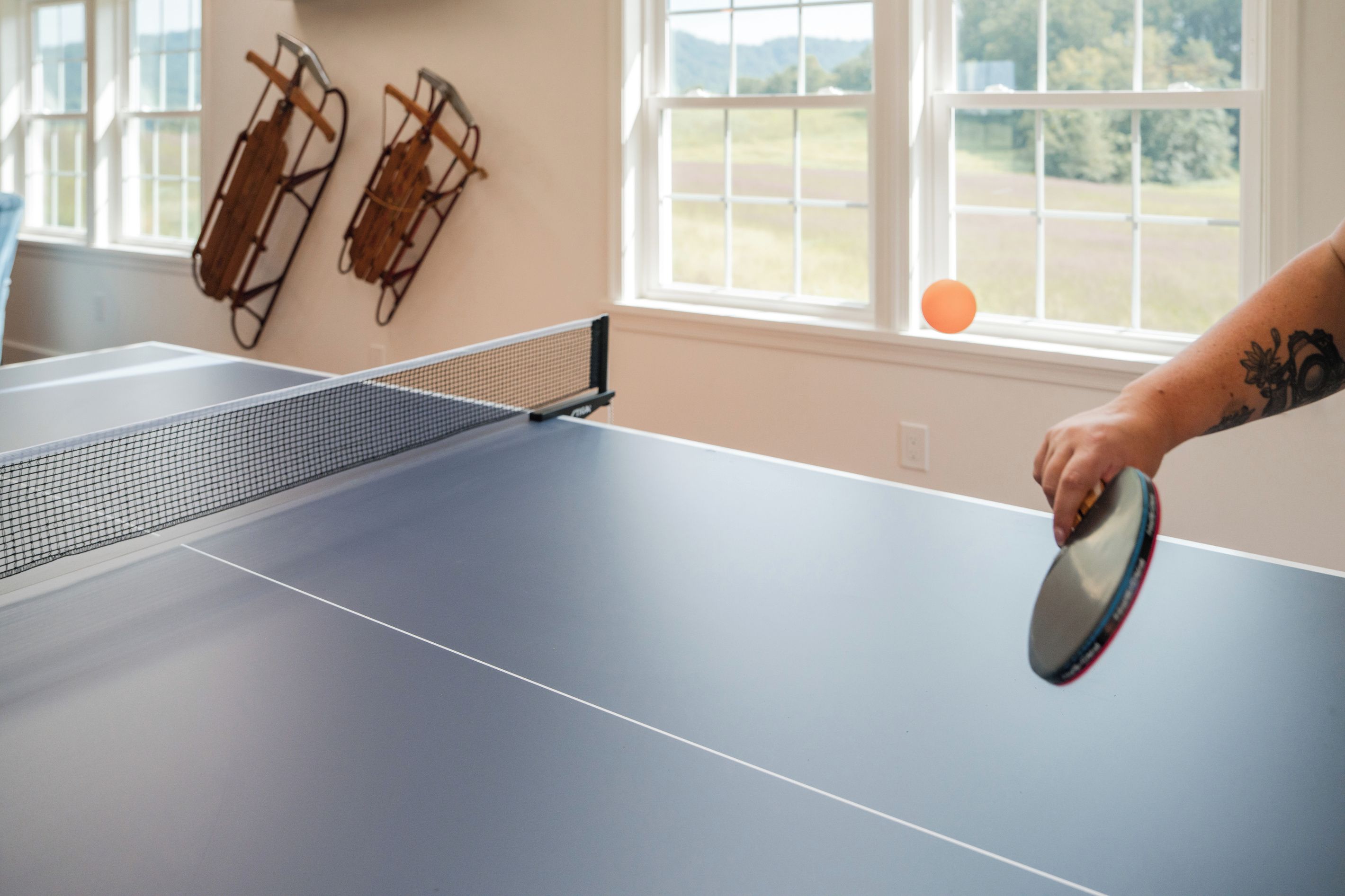 Une table de ping-pong avec un filet, dans une pièce dotée de fenêtres.