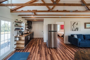 A modern kitchen with wooden beams, a stainless steel refrigerator, and a blue sofa in a living area.