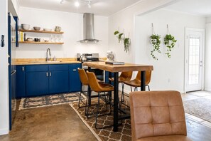 Eine moderne Küche mit blauen Schränken, einer Edelstahl-Dunstesse und einem Essbereich mit einem Holztisch und Ledersesseln.