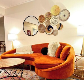 Ein Zimmer mit einem gebogenen orangefarbenen Sofa, einem runden Couchtisch und einer Wand, die mit runden gewebten Kunstwerken verziert ist.