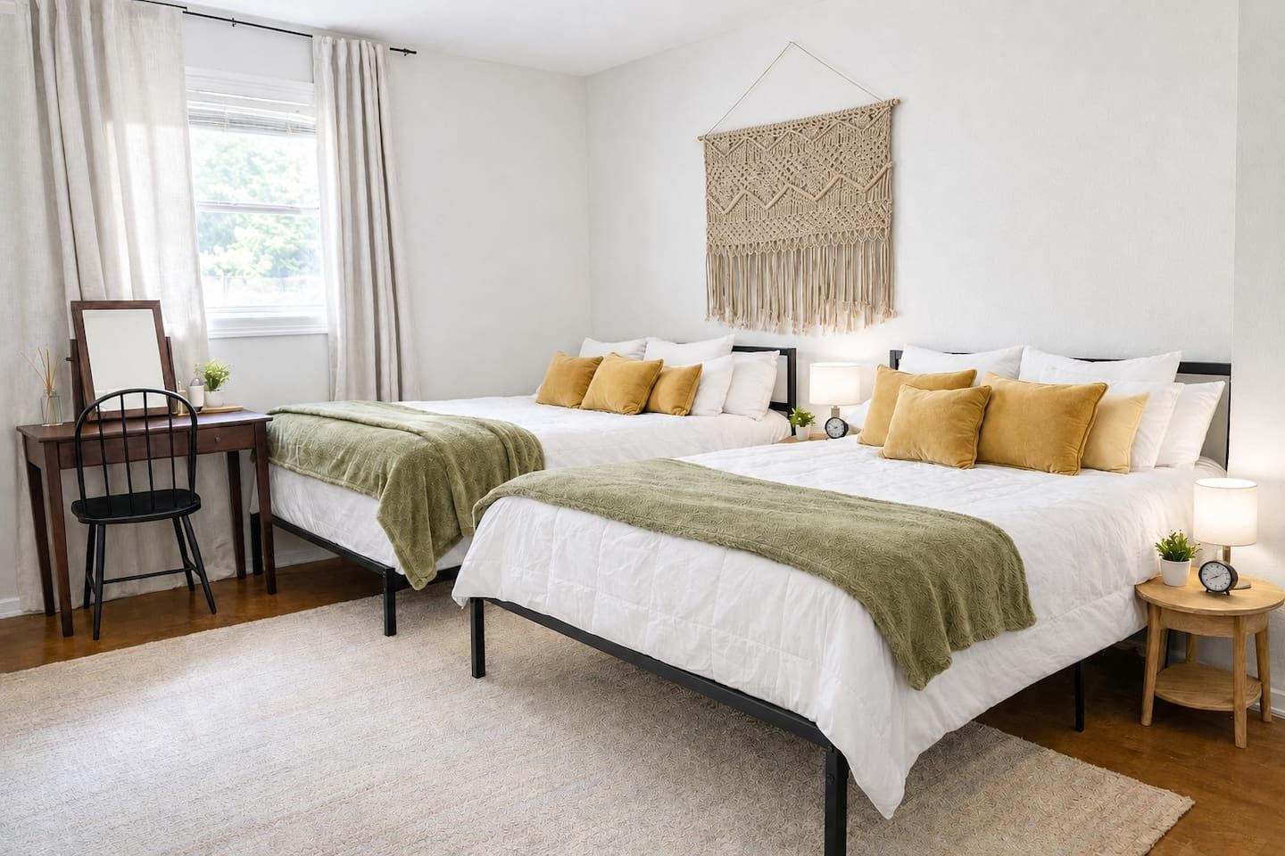 Camera da letto con due letti, una scrivania, una sedia, un comodino con una lampada e un pannello decorativo in macramè.