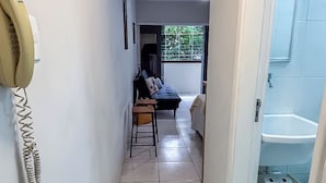 A hallway with a telephone, a sofa, and a bathroom with a sink and toilet. - SHB - Orquidário 3 min Praia em Studio (Santos)