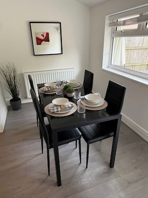 A dining area with a black table set for four, white plates, and a potted plant. - Carr Mill Stay | Free Parking | Shops & Transport (St Helens)