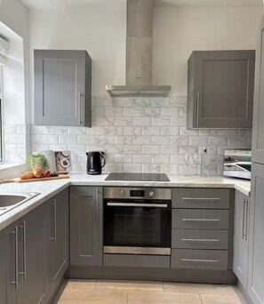 A modern kitchen with grey cabinets, a stainless steel oven, and a marble backsplash. - Carr Mill Stay | Free Parking | Shops & Transport (St Helens)