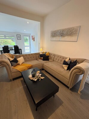 A living room with a sectional sofa, a coffee table, and a dining area in the background. - Carr Mill Stay | Free Parking | Shops & Transport (St Helens)