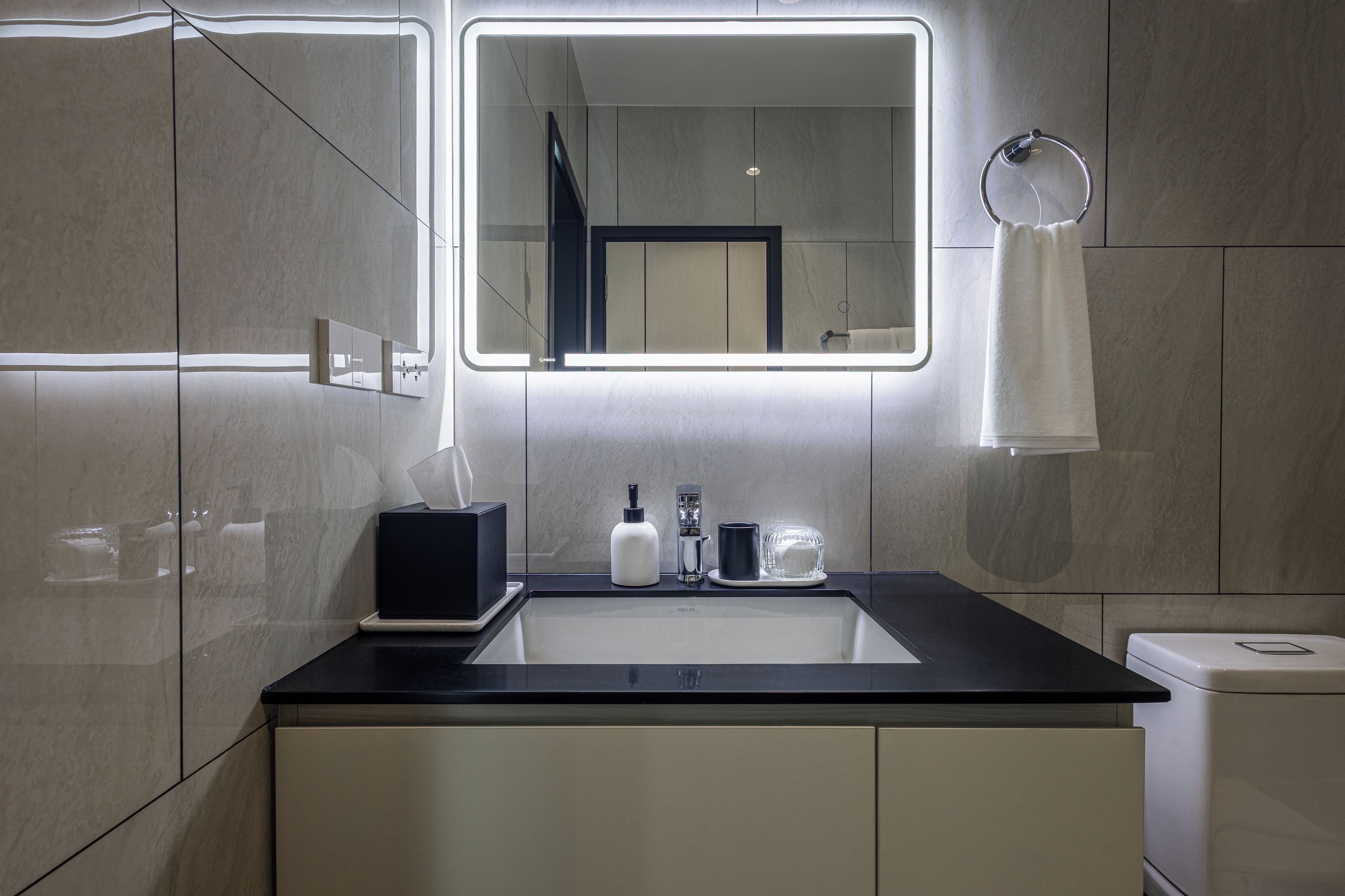 A modern bathroom with a large mirror, a black countertop, and a white sink.