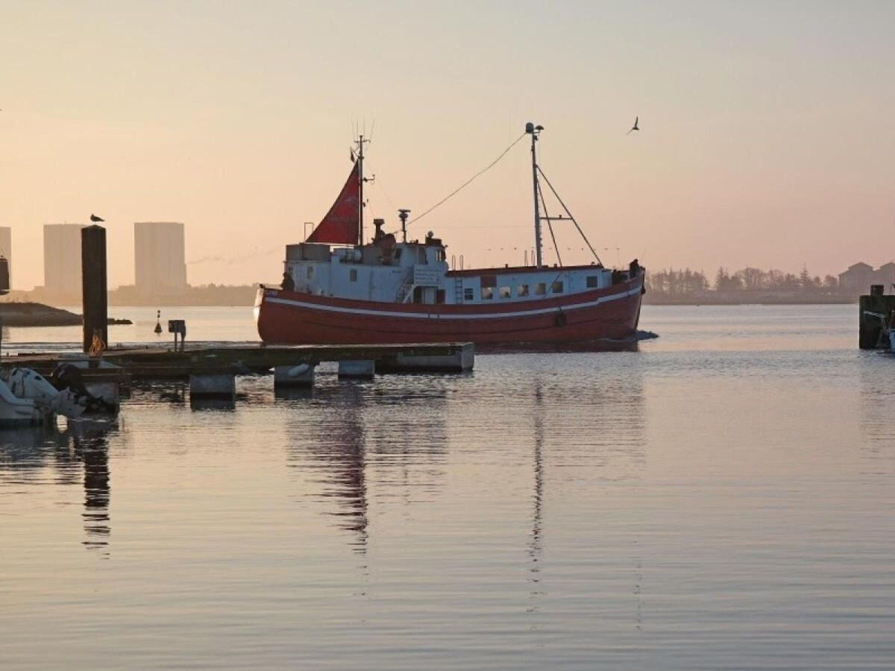 A red boat docked at a pier with calm water and a clear sky.
