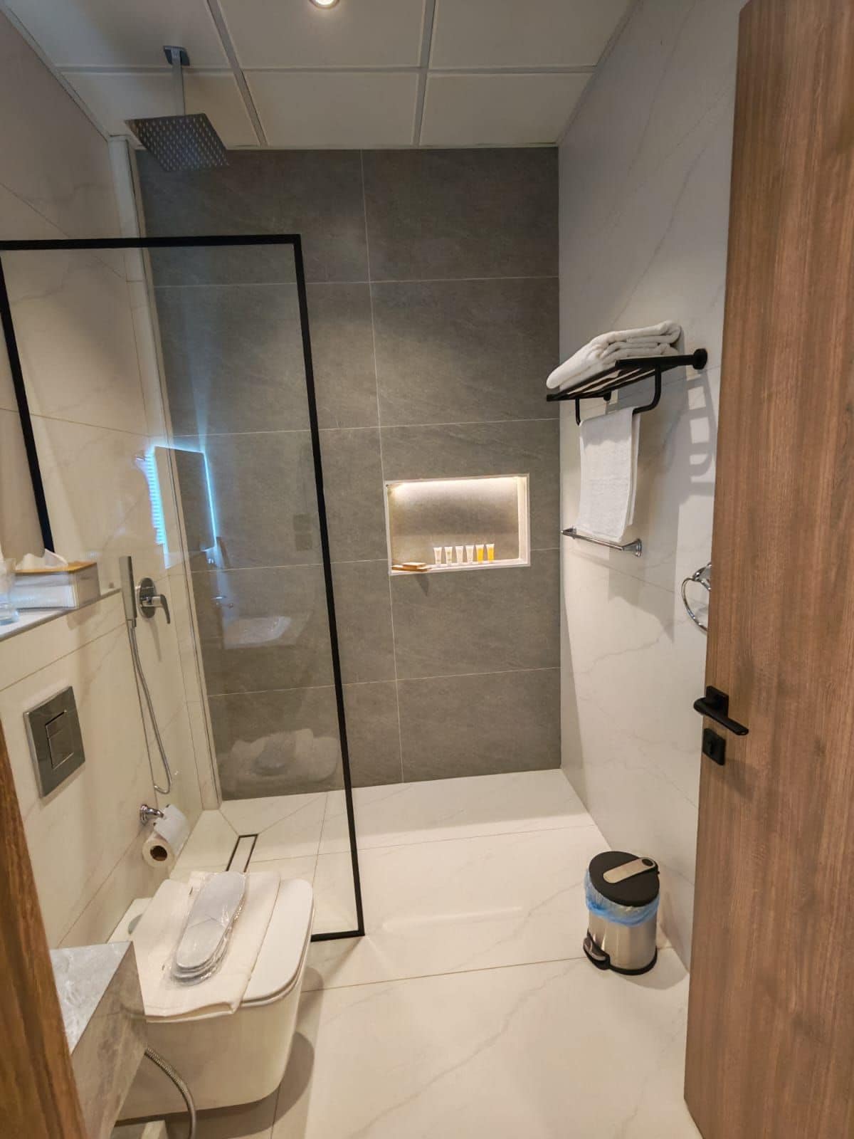 Un baño moderno con ducha envuelta en cristal, inodoro, lavamanos y perchero para toallas.