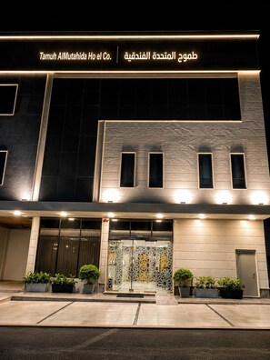 A modern building facade with illuminated signage in both English and Arabic, featuring a geometric pattern at the entrance. - tamouh almuttahida hotel (Madinah)