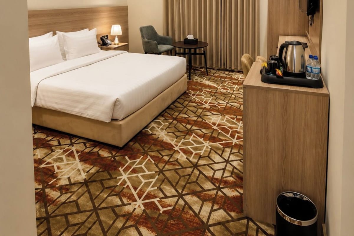 Une chambre d’hôtel équipée d’un lit, d’un bureau, d’une chaise, d’une télévision et d’une moquette à motifs.