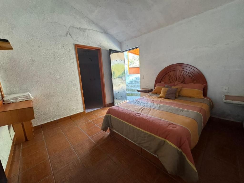 Ein Schlafzimmer mit einem Bett, einem Nachttisch aus Holz, einer Tür zu einem Außenbereich und einem gefliesten Boden.