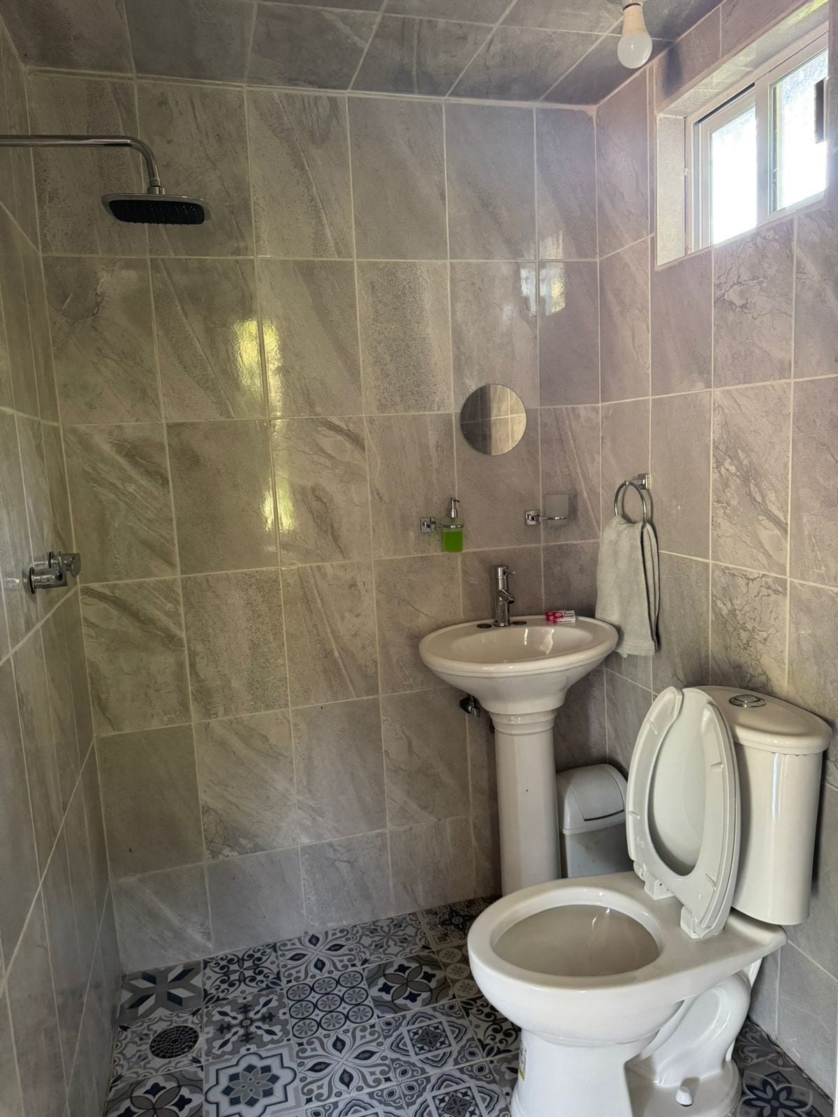 Un baño con ducha, lavamanos, inodoro y baldosas de suelo estampadas.