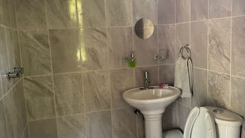 Un baño con ducha, lavamanos, inodoro y baldosas de suelo estampadas.